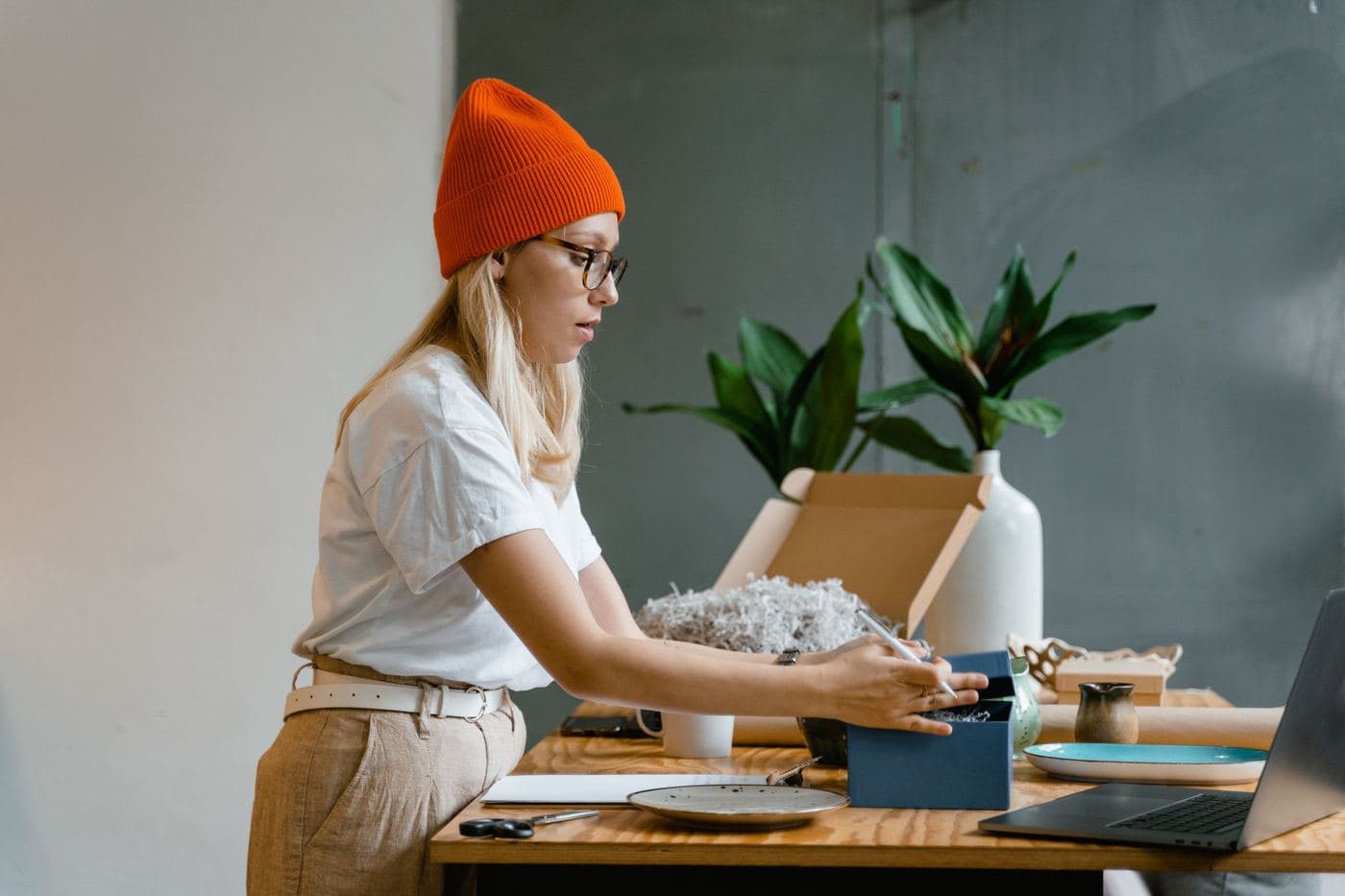 Persona con gorro preparando un pedido de su tienda online junto a plantas y una laptop